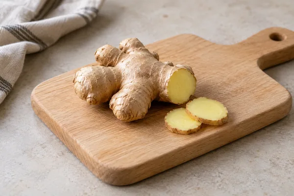 Frische Ingwerknolle mit zwei Scheiben auf einem Holzbrett