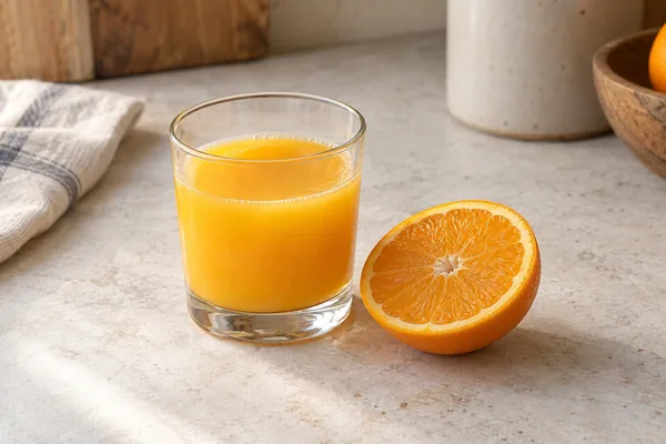 Kleines Glas Orangensaft neben einer Orangenhälfte